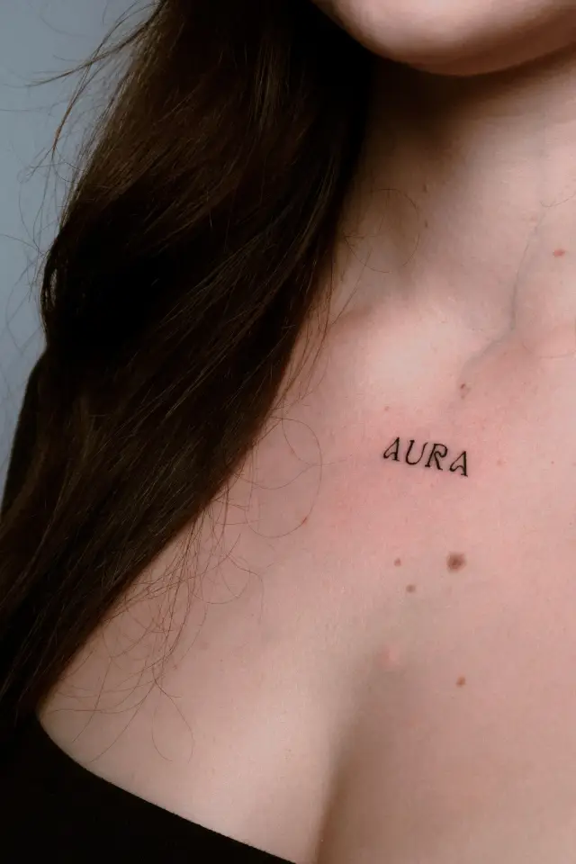 Fine line tetovaža natpisa „AURA” na ključnoj kosti, freshly tattooed
