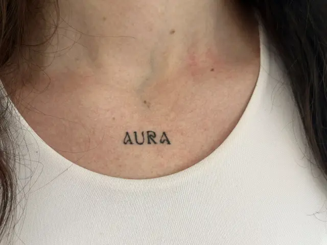 Fine line tetovaža natpisa „AURA” na ključnoj kosti, healed